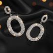 Pair of silver hoop earrings with clear gemstones on a black fabric background.