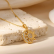 Gold necklace with sun and moon pendant on a textured beige surface
