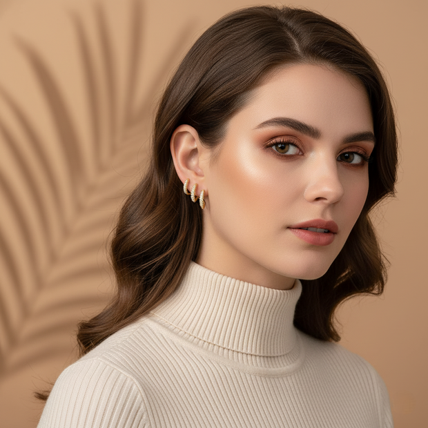 A woman wearing a pair of yellow gold-tone claw stud wrap earrings with cubic zirconia. against a brown background