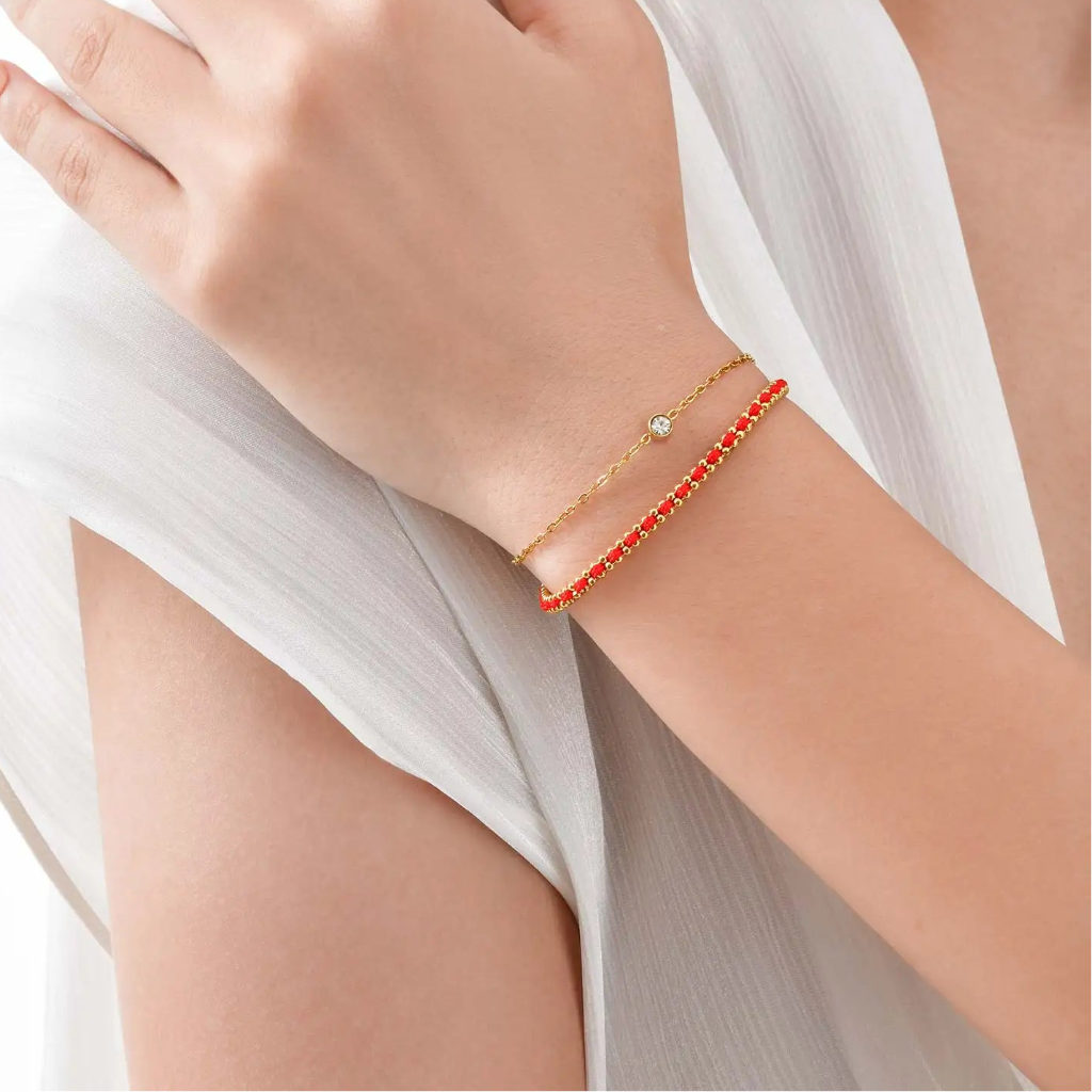 Hand wearing a red beaded bracelet with a gold chain on a white background