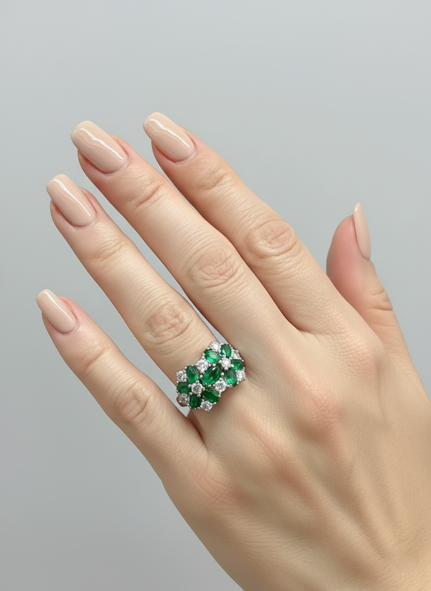 Hand wearing a ring with emeralds and diamonds on a gray background