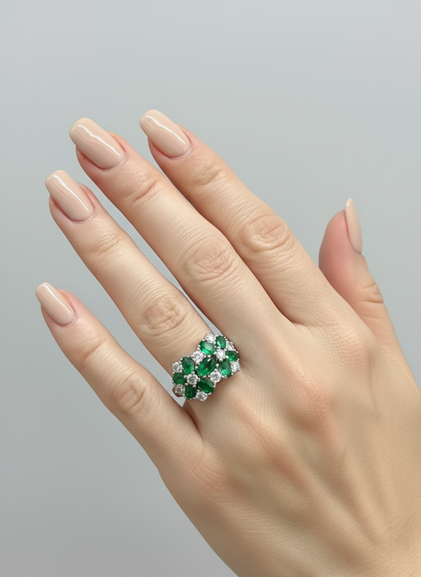 Hand wearing a ring with emeralds and diamonds on a gray background