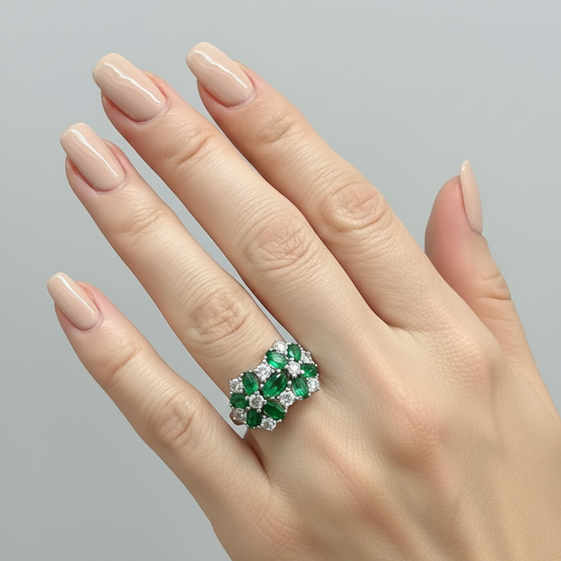 Hand wearing a ring with emeralds and diamonds on a gray background