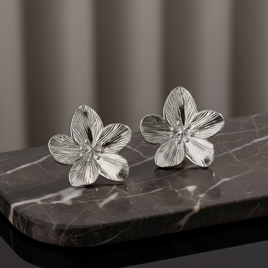 Silver flower-shaped earrings on a dark marble surface with a blurred background