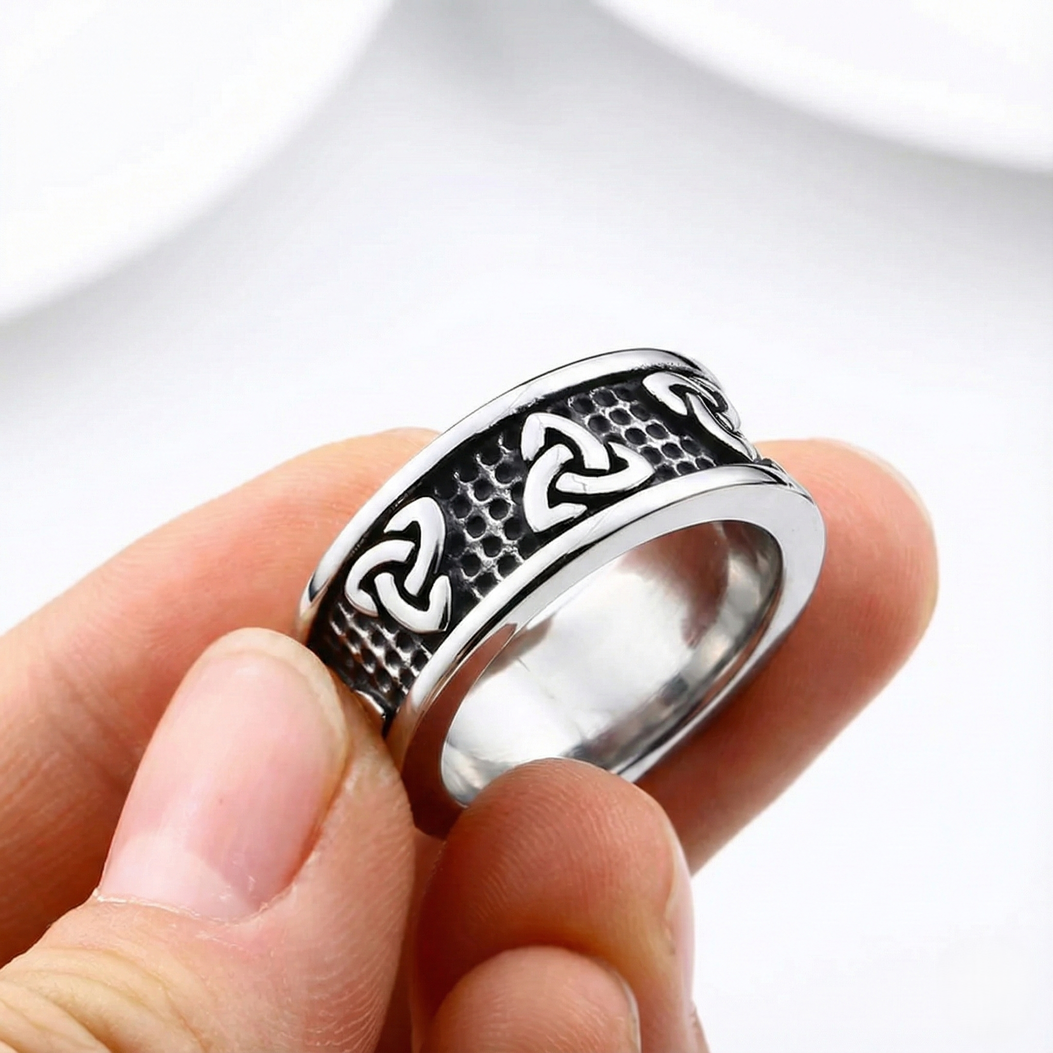 Silver trinity knot ring with intricate design held between fingers on a white background