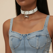 Person wearing a denim dress with a white choker and dog tag on a beige background